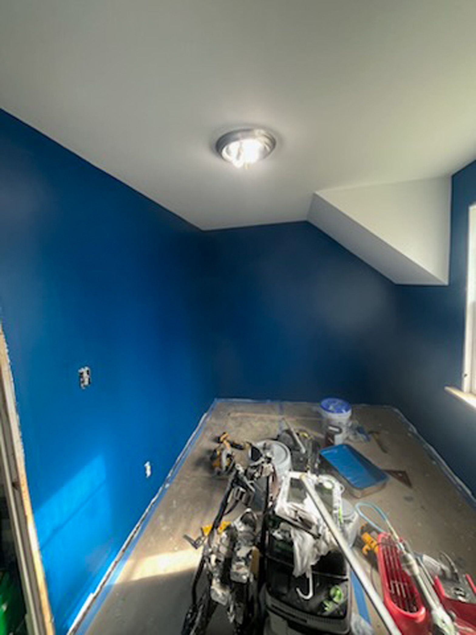 A room with blue walls and white trim is being painted.