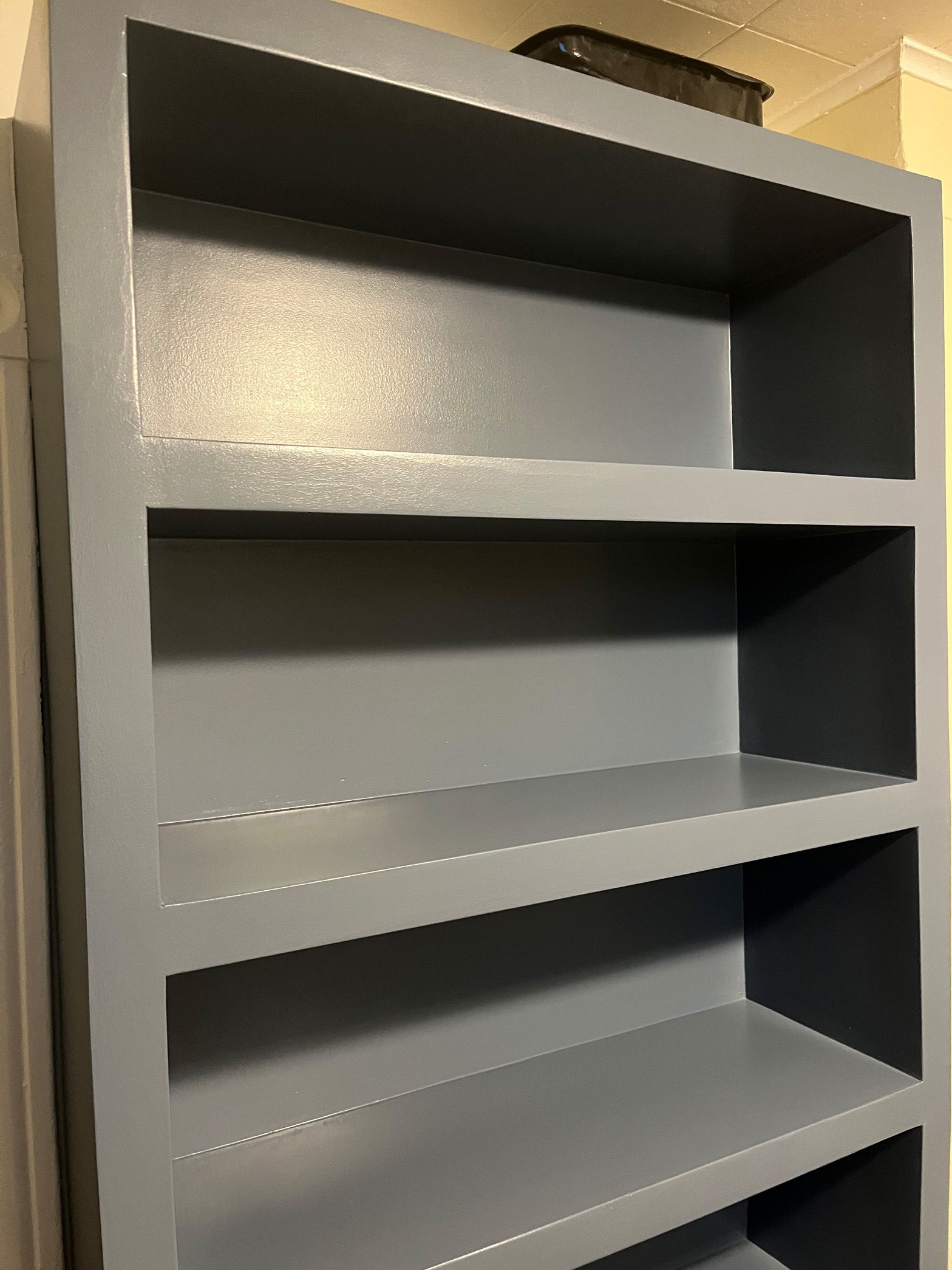 A gray bookshelf with four shelves in a room.