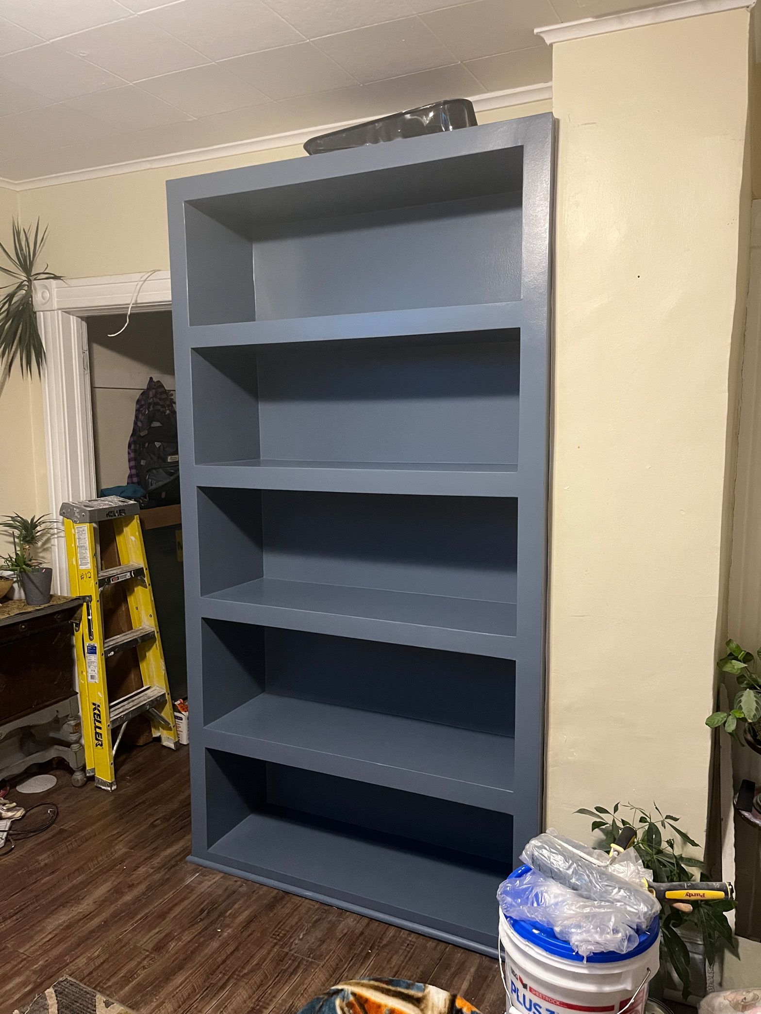 An empty bookshelf is sitting in a living room next to a ladder.