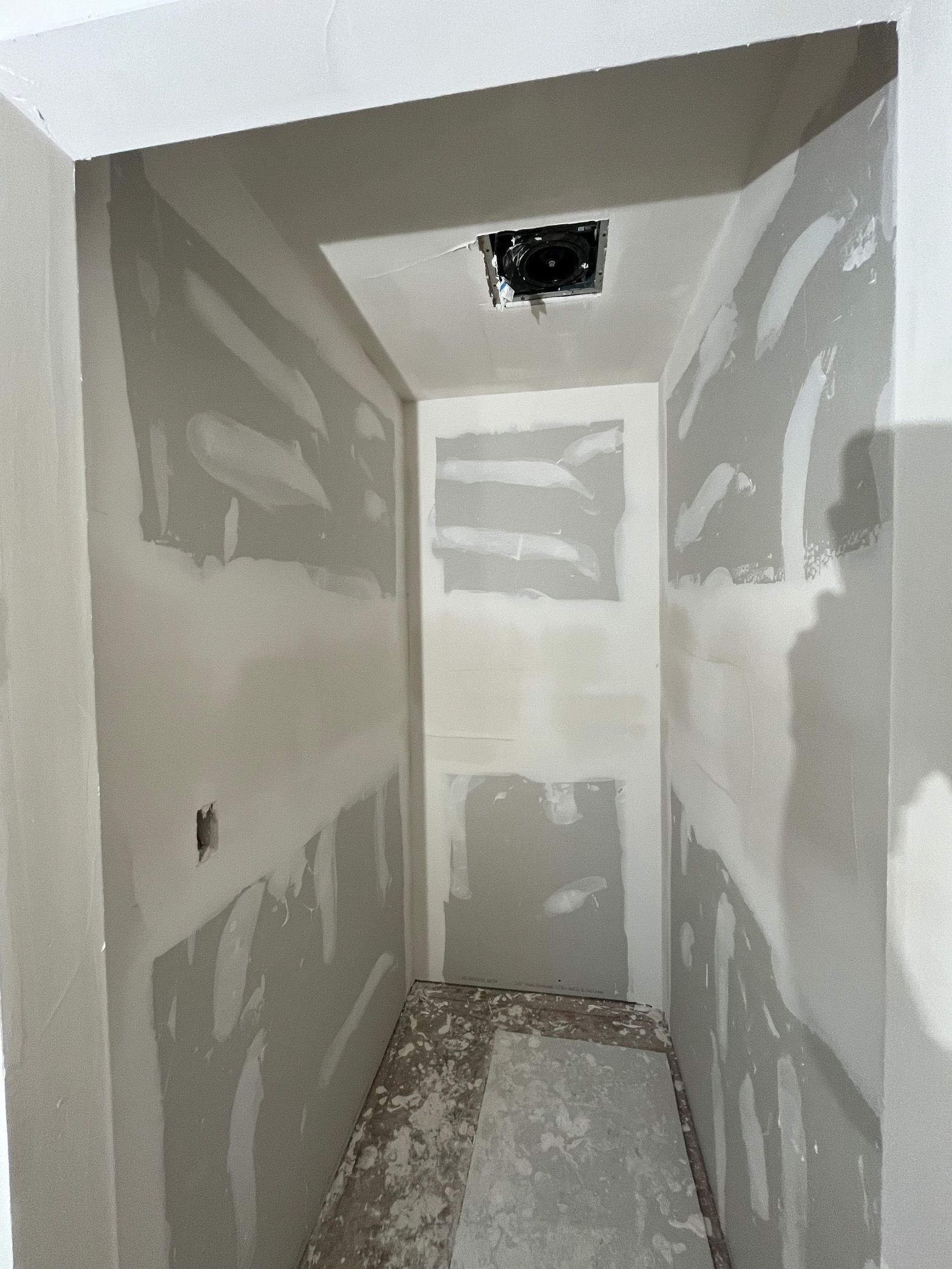 A hallway with drywall walls and a ceiling fan