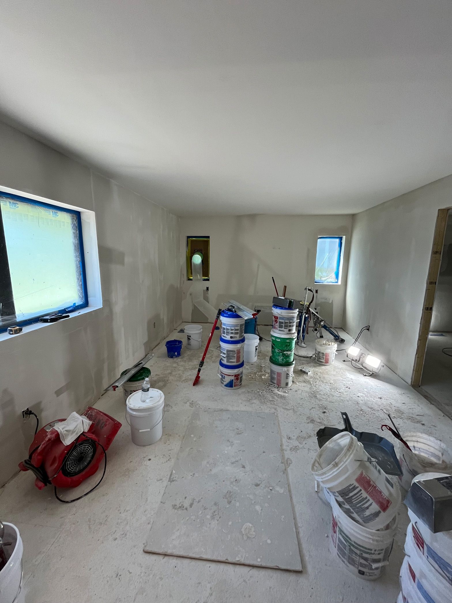 A room with buckets of paint and a fan on the floor.