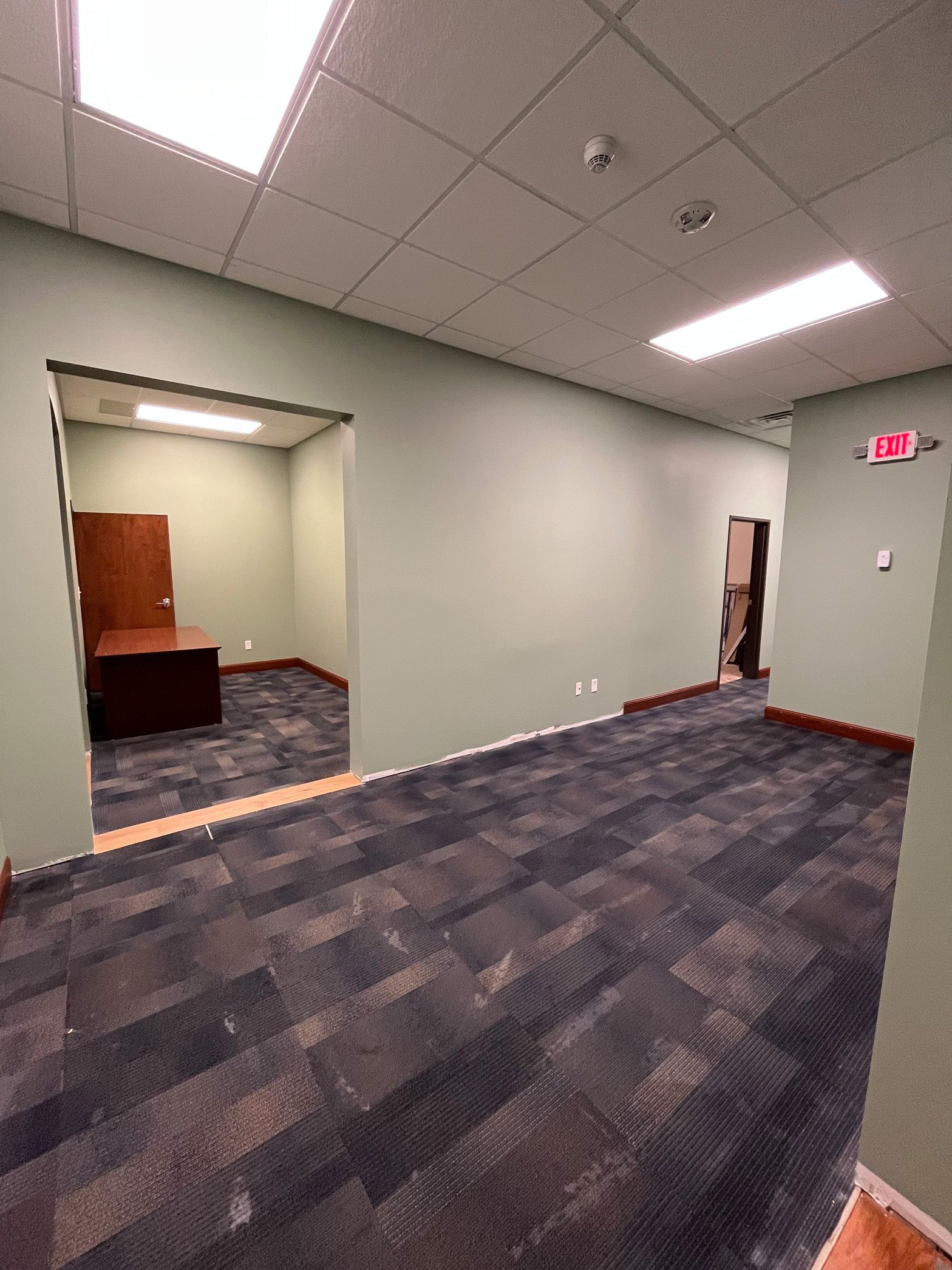 A large empty room with a carpeted floor and a desk.