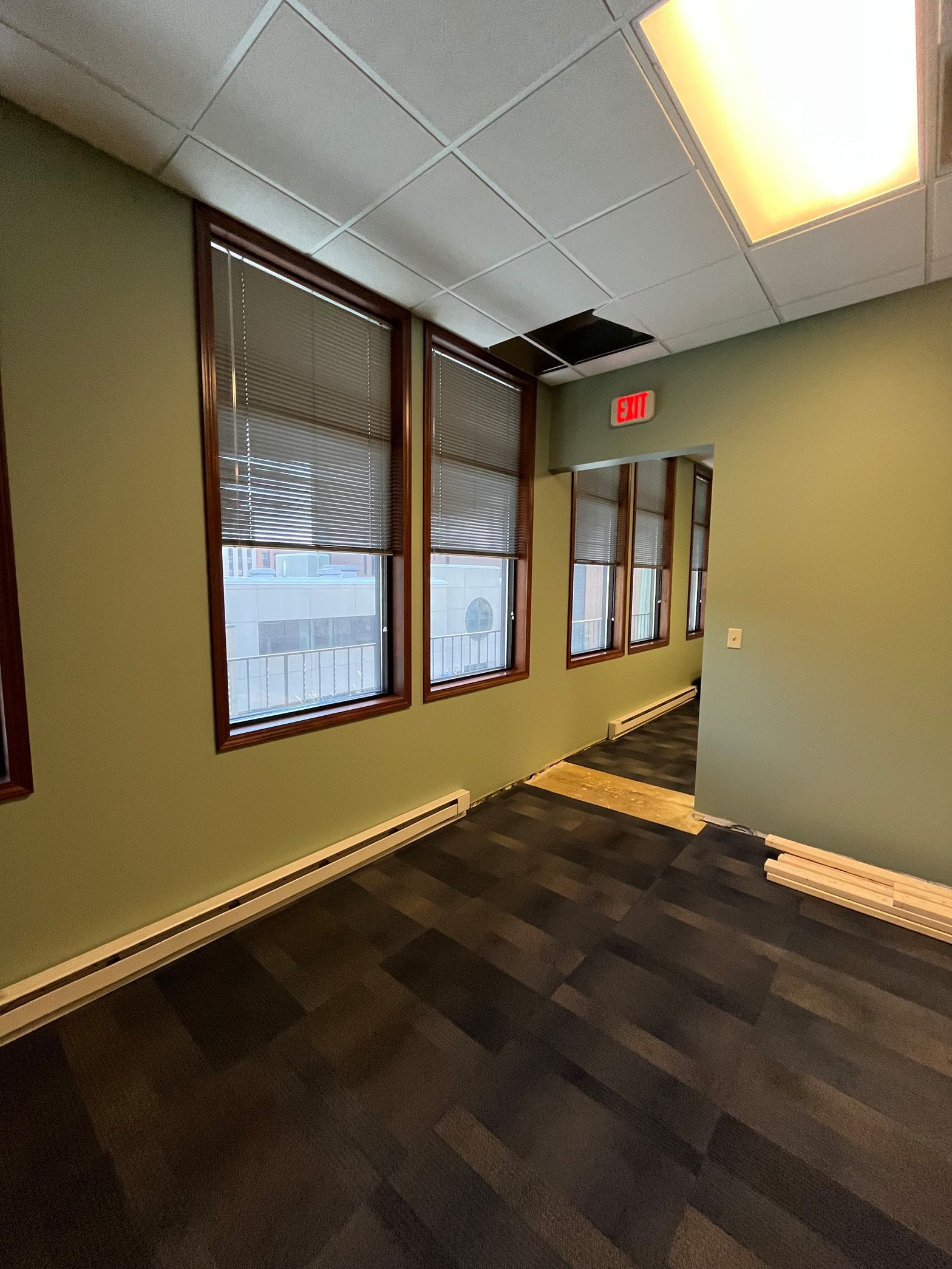 An empty room with a lot of windows and a red exit sign.