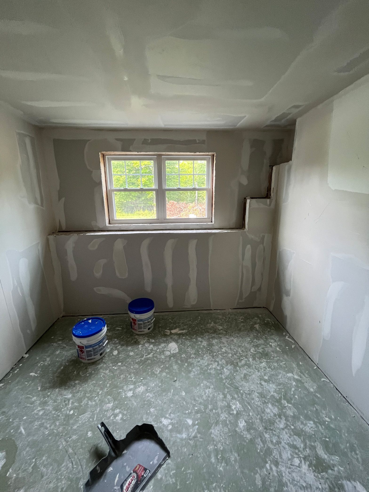 A room with a window and buckets of paint on the floor.