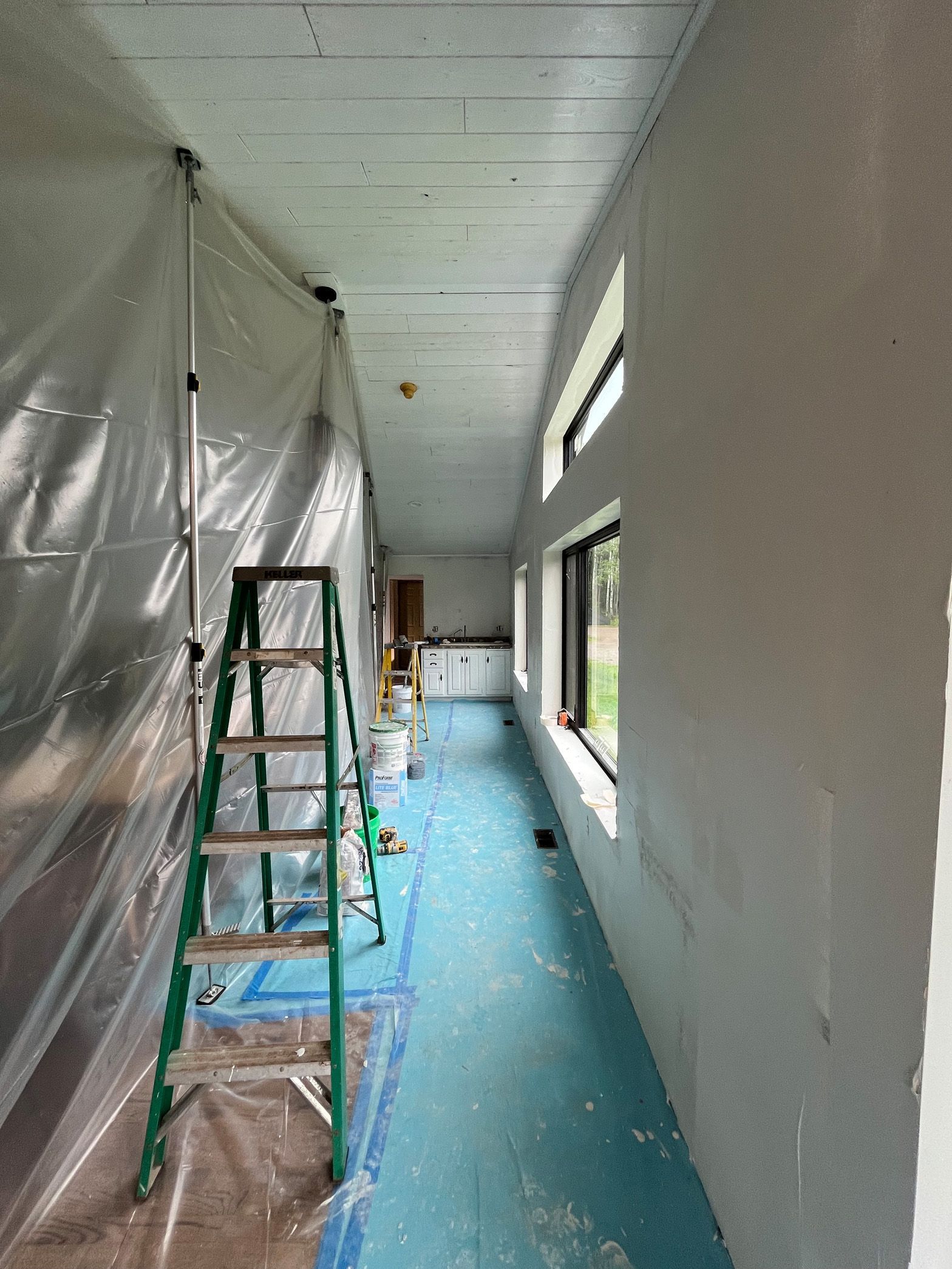A long hallway with a ladder and a plastic sheet on the wall.