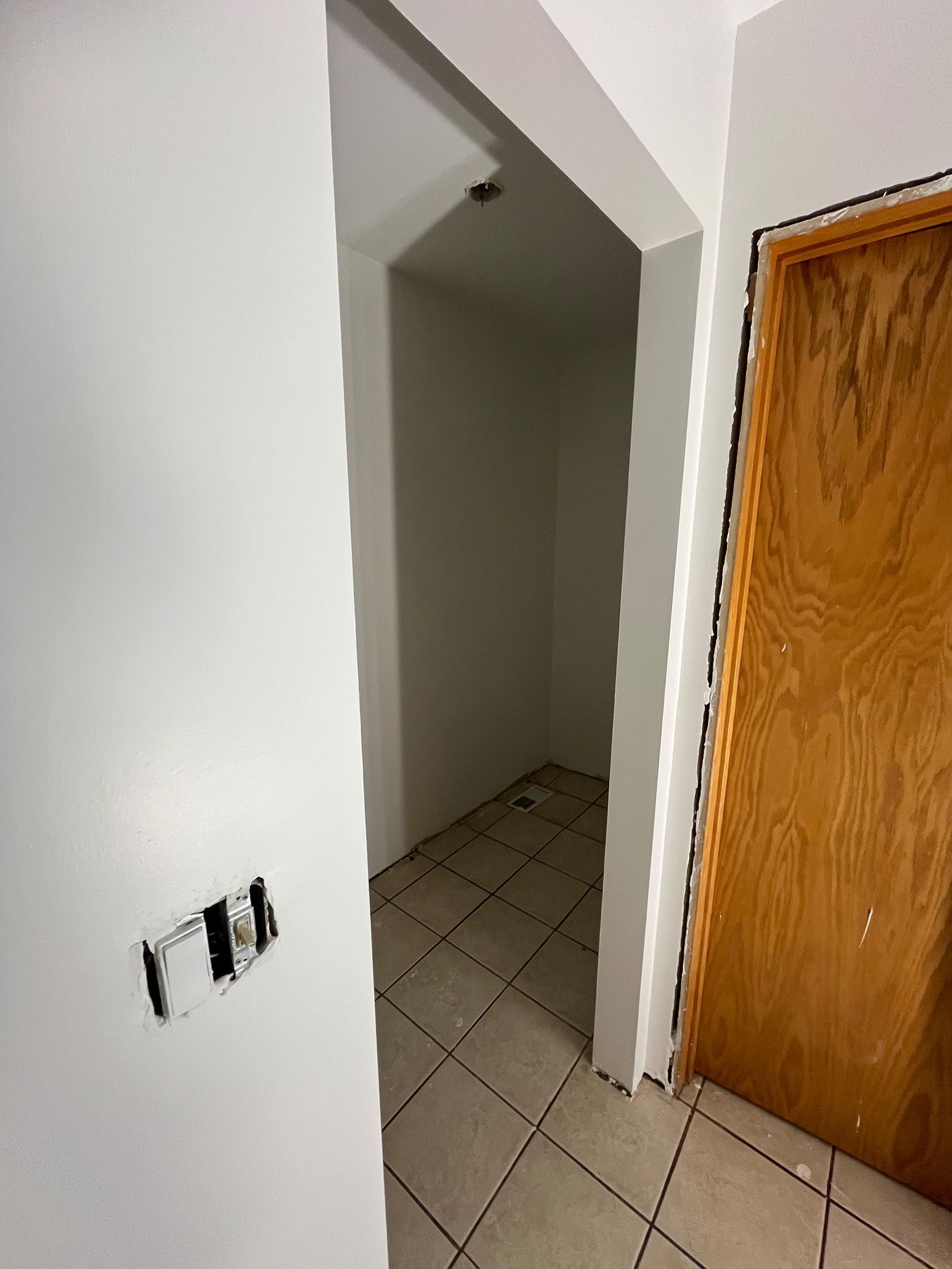 A hallway with a wooden door and a tiled floor.