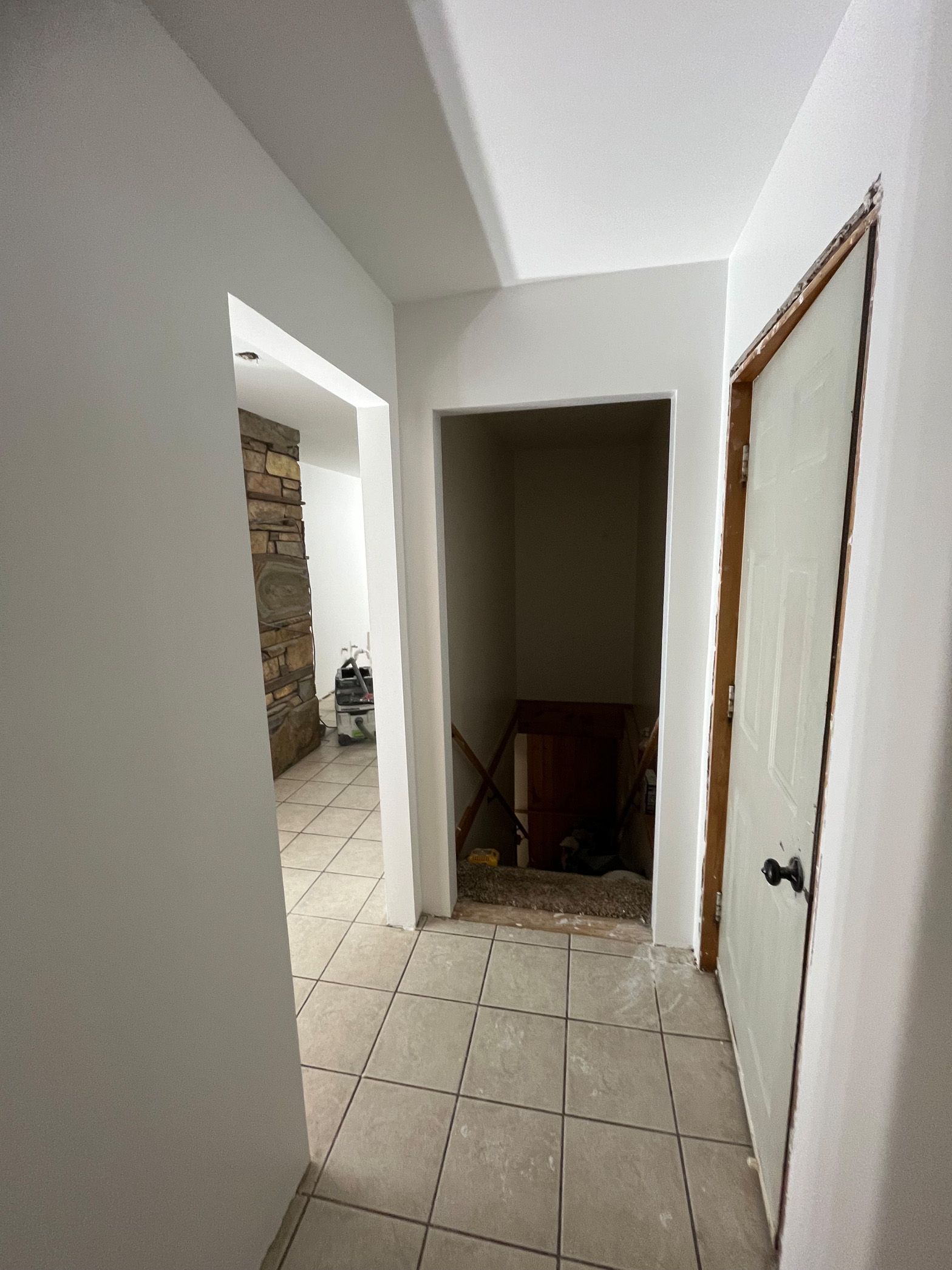 A hallway with white walls and tile floors and a door.