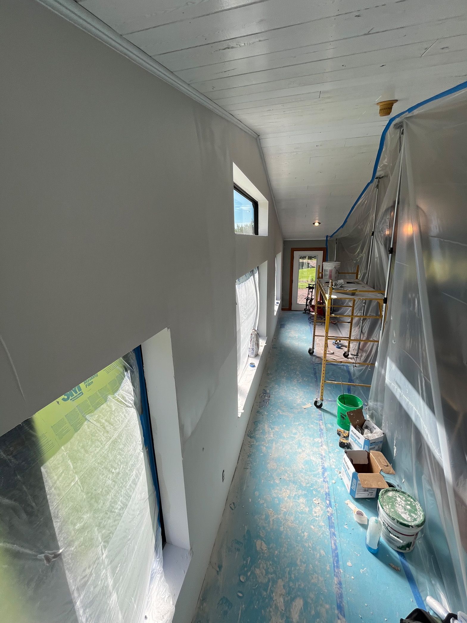 A long hallway with a lot of windows is being painted.