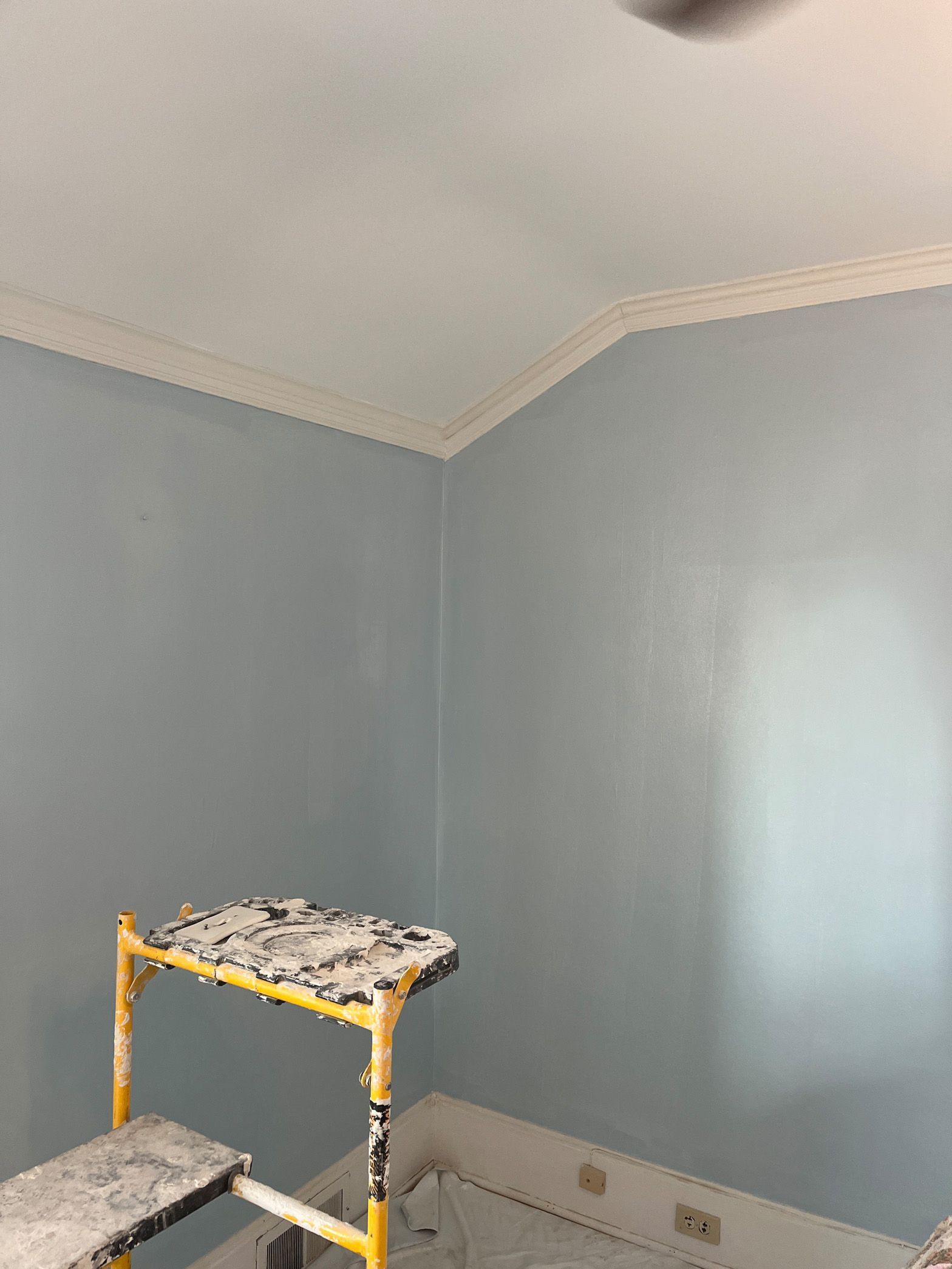 A room with blue walls and a ceiling fan is being painted.