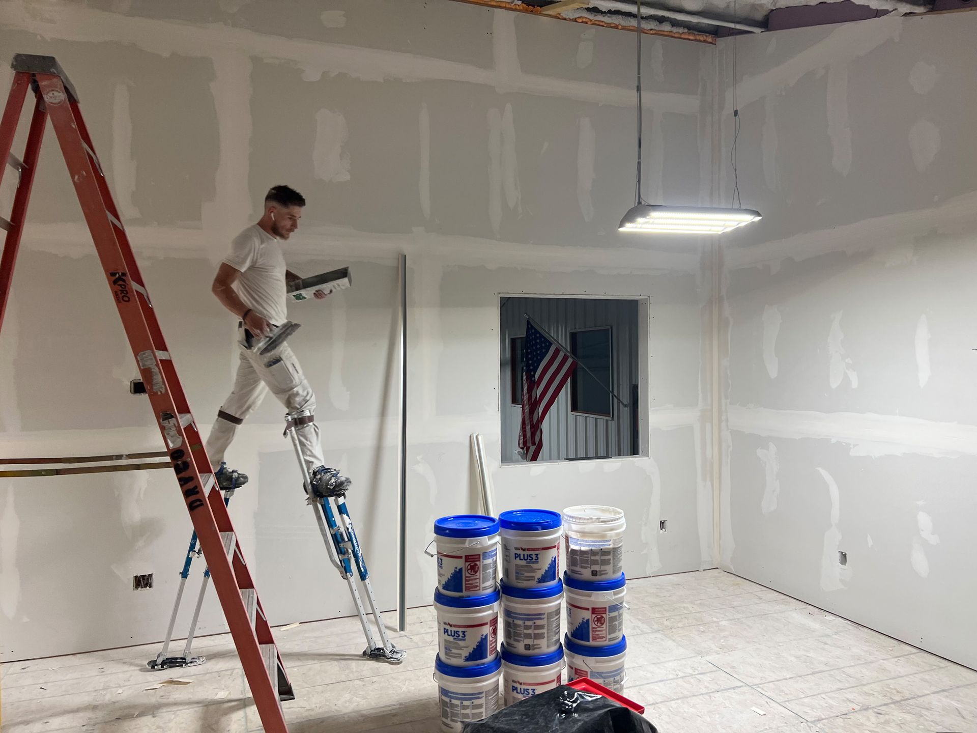 A man is standing on a ladder in a room painting a wall.