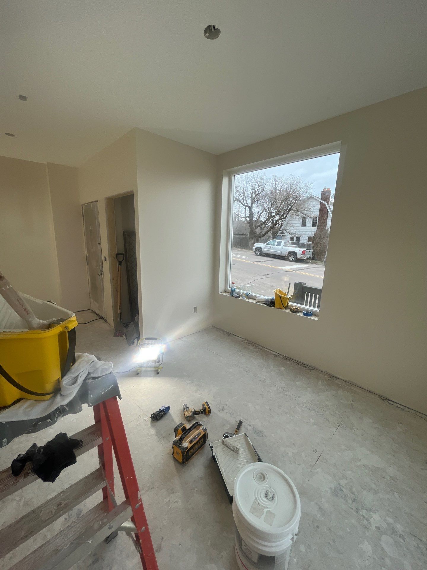 A room with a window and a bucket of paint on the floor.