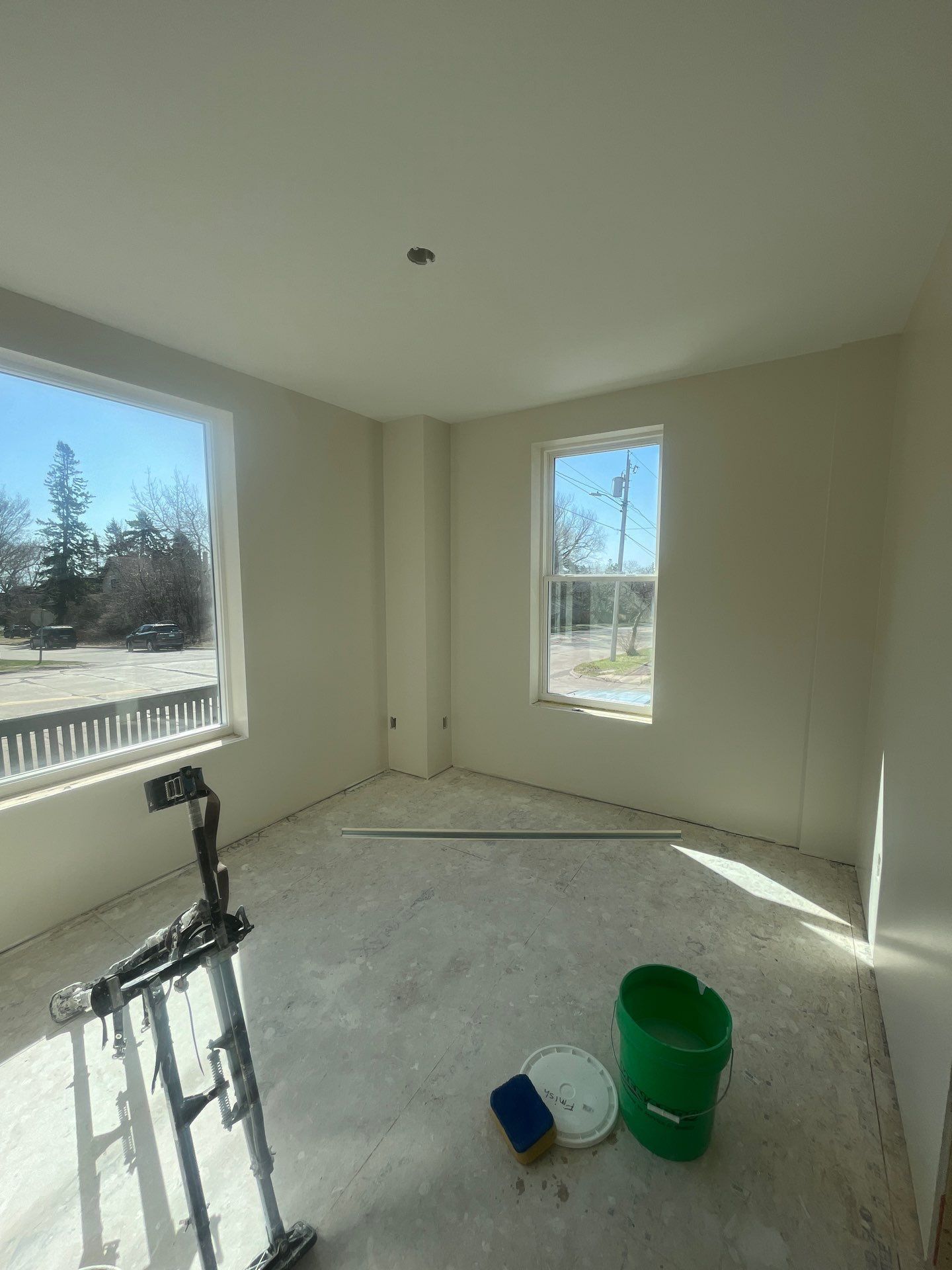 An empty room with two windows and a green bucket on the floor.