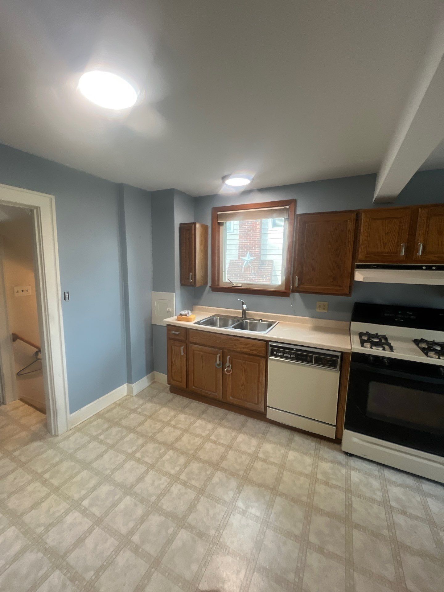 A kitchen with wooden cabinets , a stove , a sink , and a window.