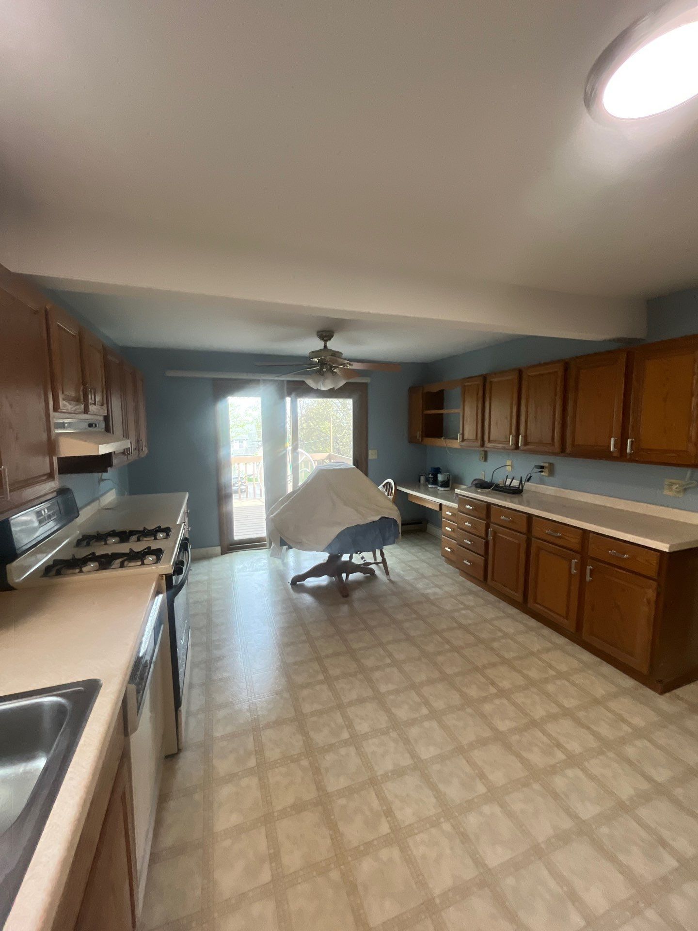 A kitchen with wooden cabinets , a stove , a sink , and a ceiling fan.