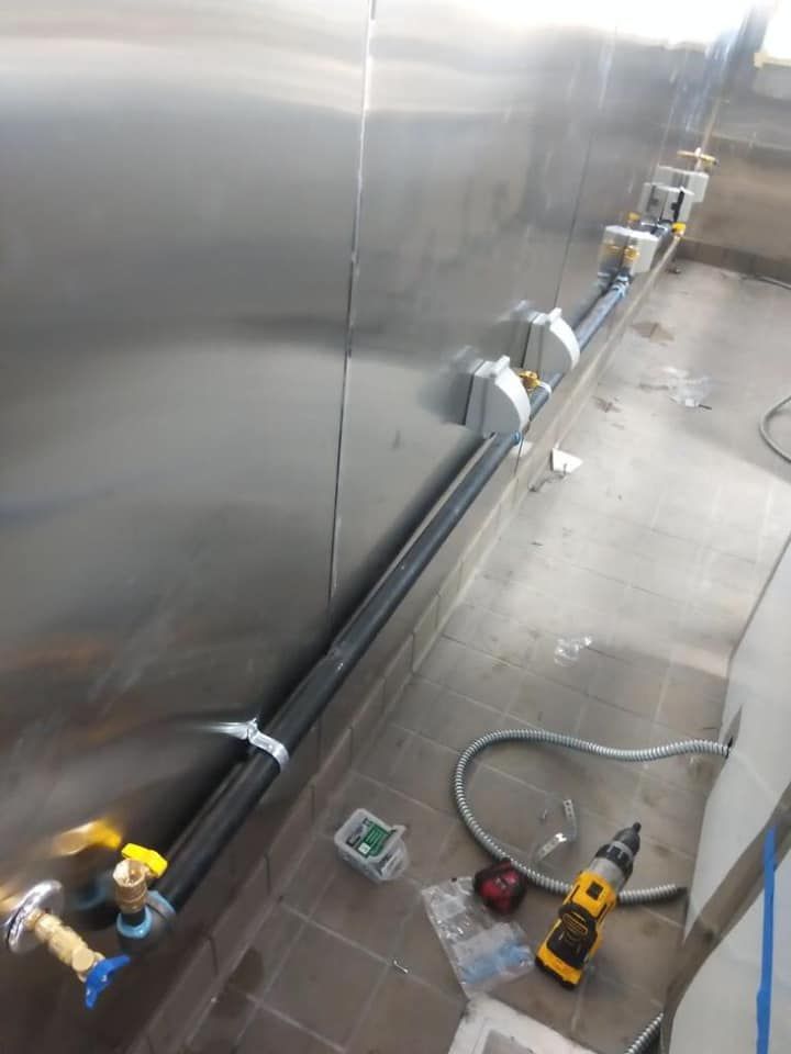 A stainless steel wall with pipes and a drill on the floor.