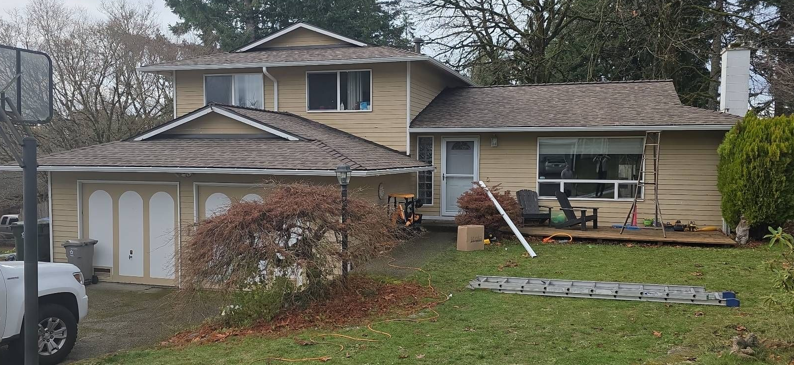 Beige two-story house with a garage and a yard with a ladder against the side.