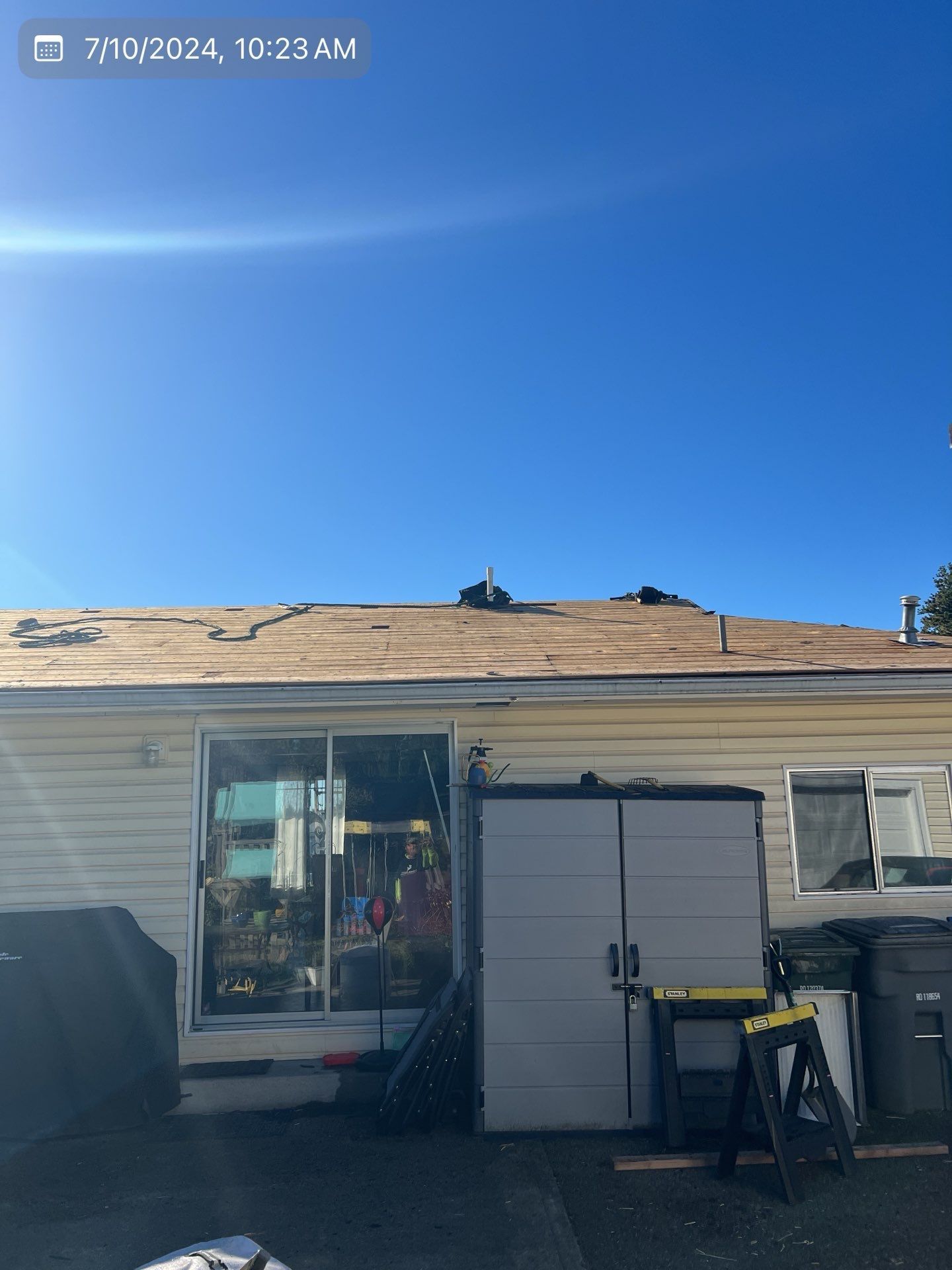 Backyard view: partially torn roof, sliding glass door, white shed, blue sky.