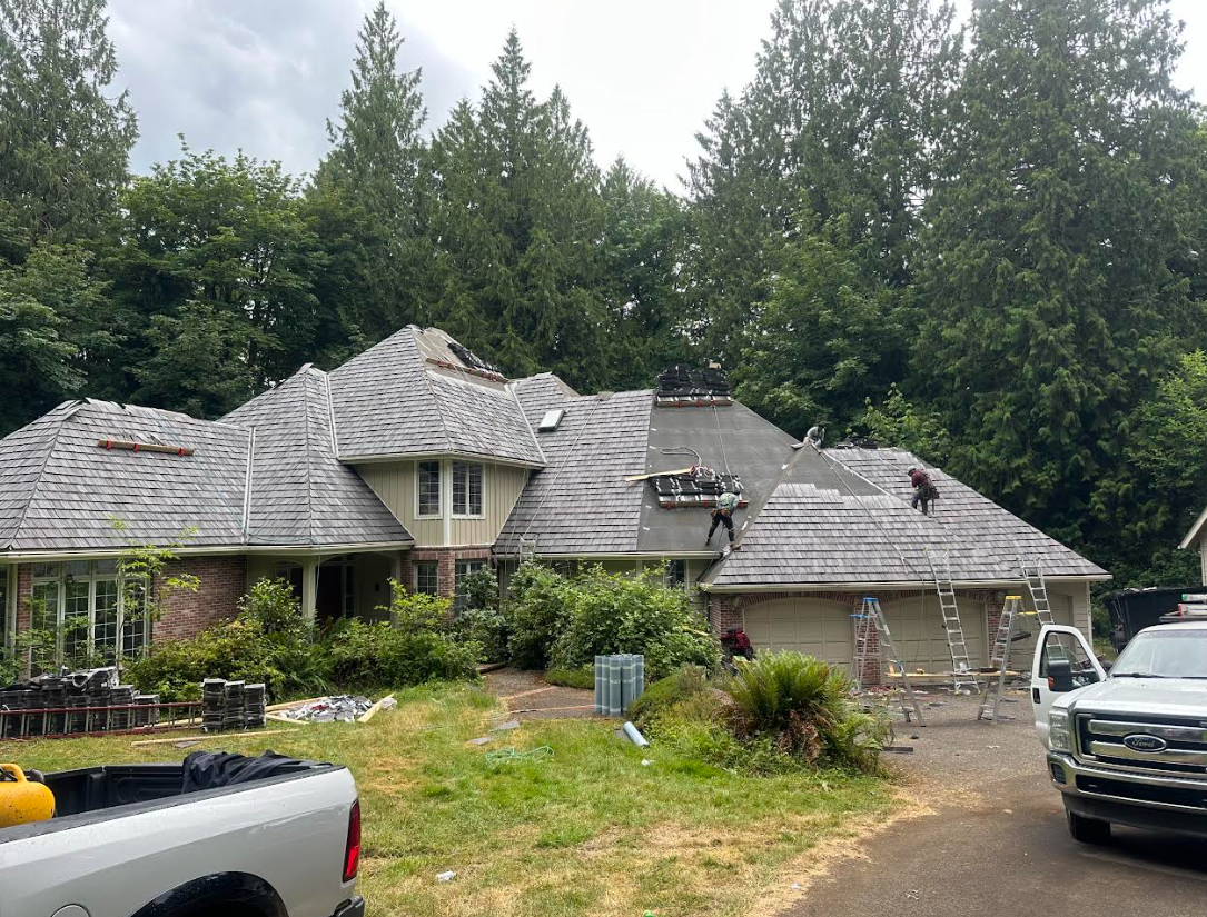 Roofers working on a house with gray cedar Brava shingles. Trees surround the home.