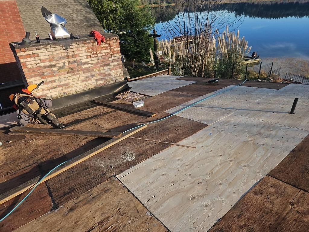Rooftop with plywood being installed. Chimney with brickwork, lake in background.