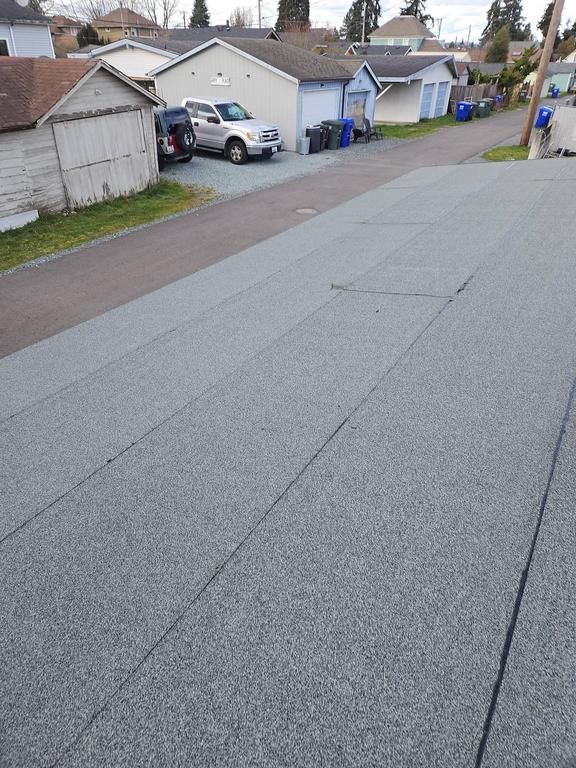 View from rooftop of asphalt shingle roof, looking down at a street with parked cars and garages.
