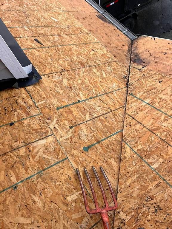 Close-up of a roof under construction showing plywood sheathing, a flashing, and a gardening fork.
