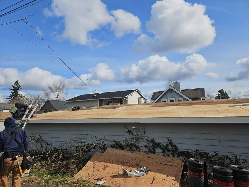 Roofing work on a flat roof under a blue sky with puffy clouds. A worker is near the ladder in Everett, WA.