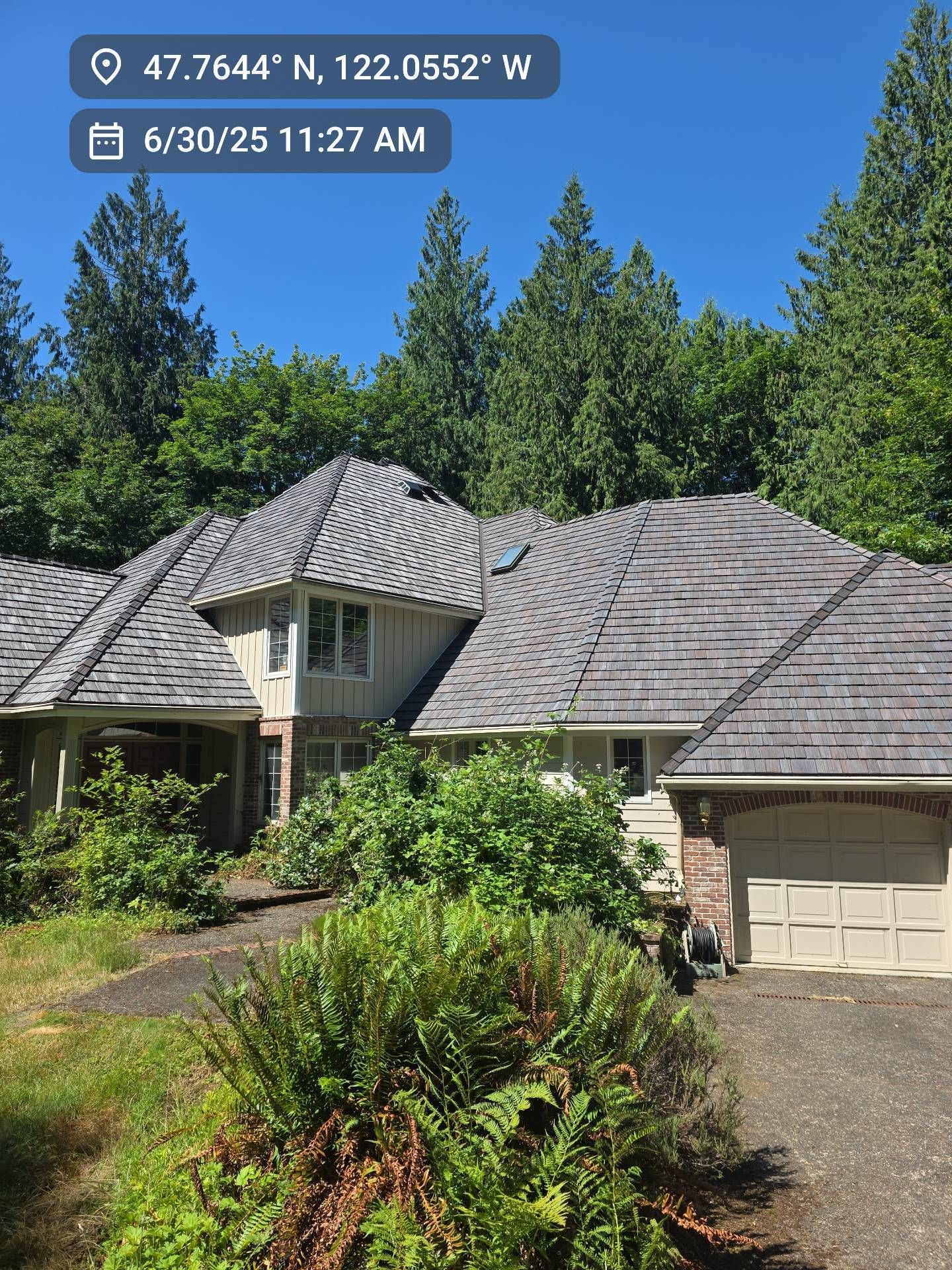 House with multiple rooflines, surrounded by greenery under a bright sky. Beige garage door visible.