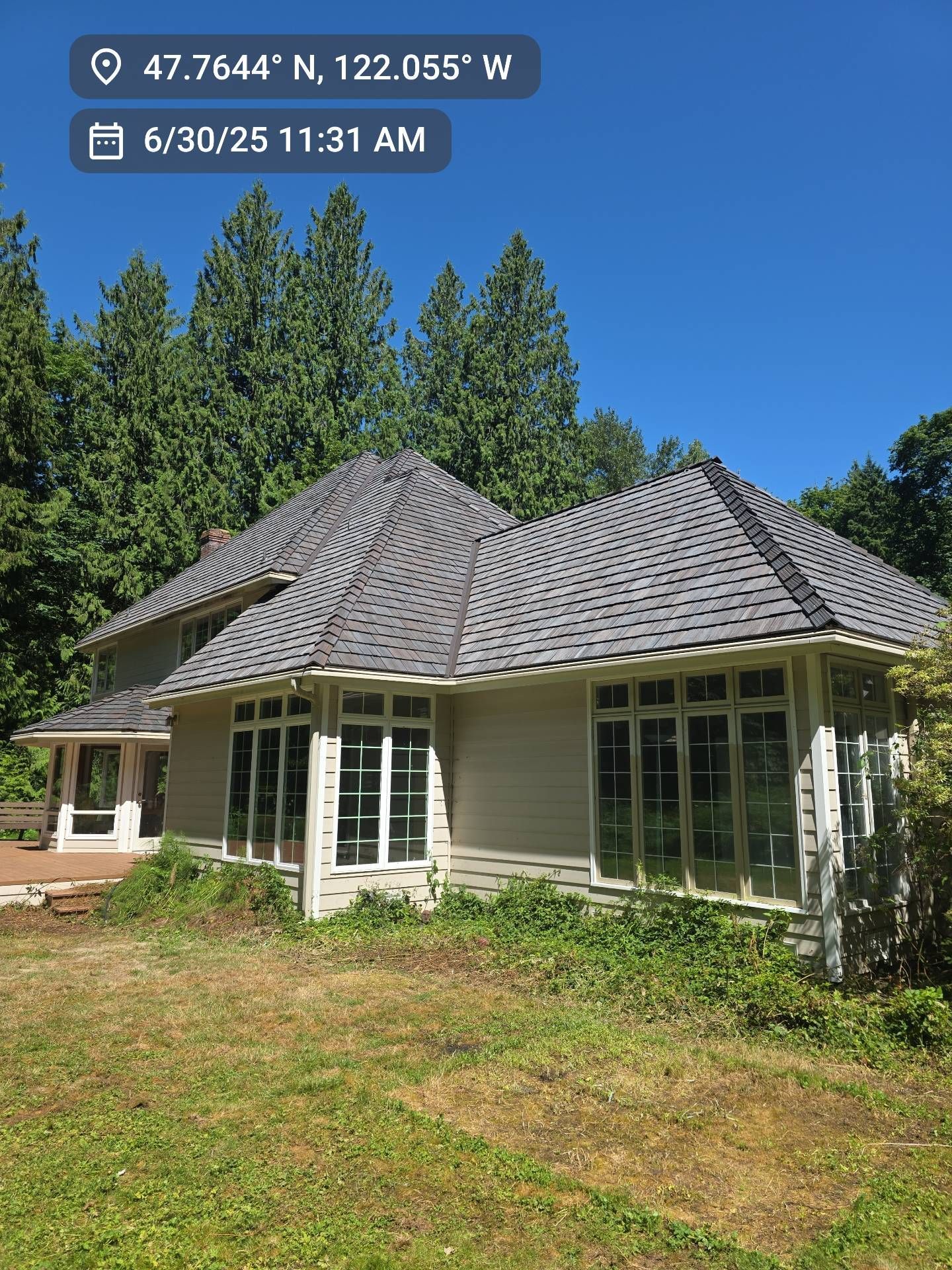 Light-colored house with Brava Cedar Tile, surrounded by trees and overgrown vegetation.