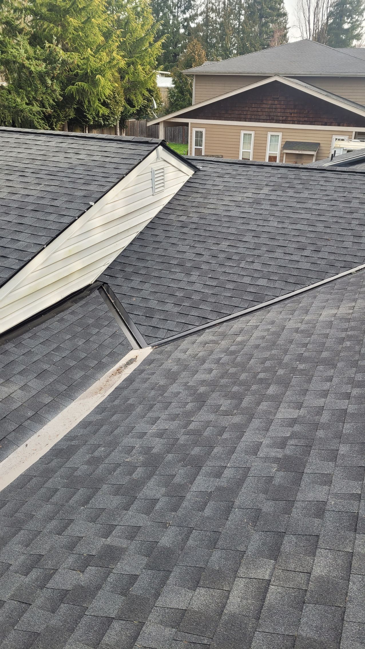 Close-up of a dark asphalt shingle roof with a light-colored metal flashing at a joint.
