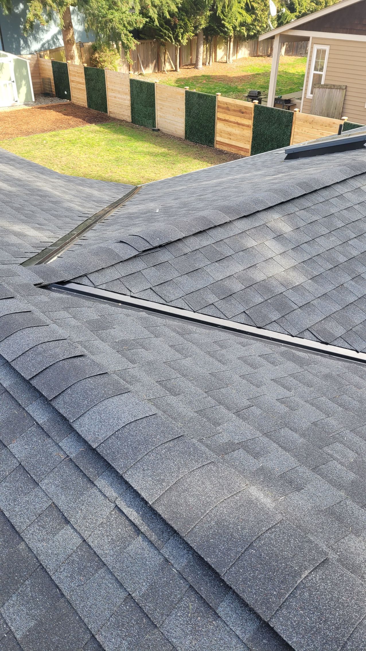 View from a roof of asphalt shingles. A metal flashing runs through the center.