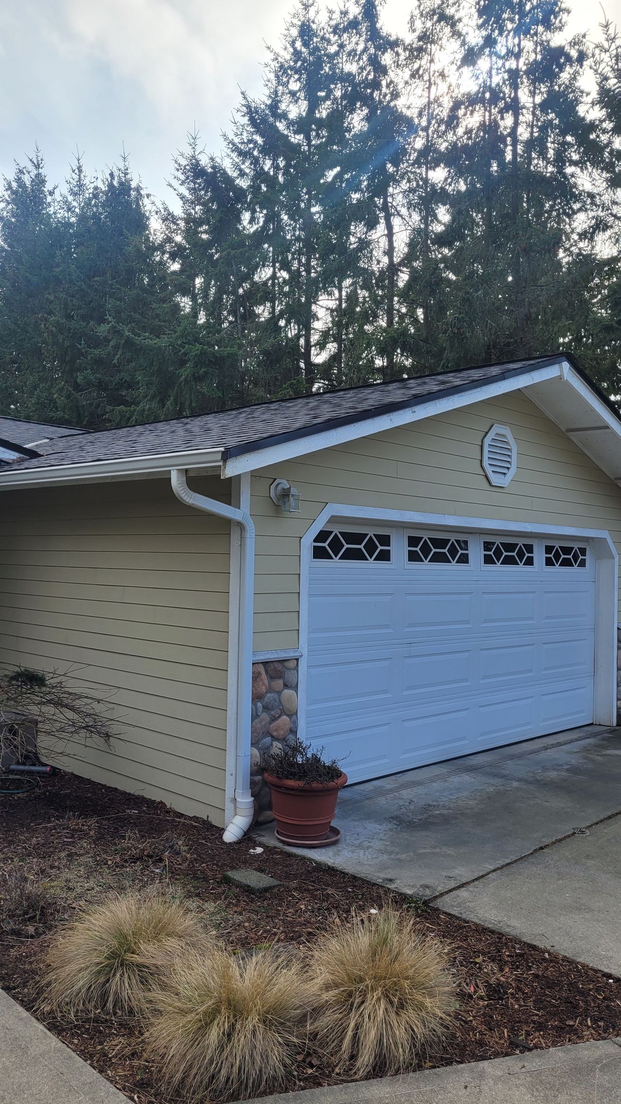 Yellow house with white garage door and trees in background.