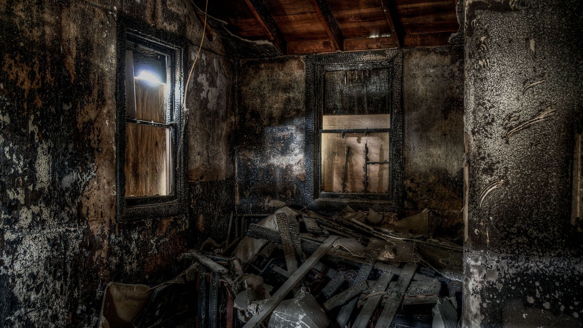 Interior of a burnt room: charred walls and debris, two windows letting in light.
