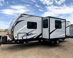 A white and blue travel trailer is parked in a parking lot.