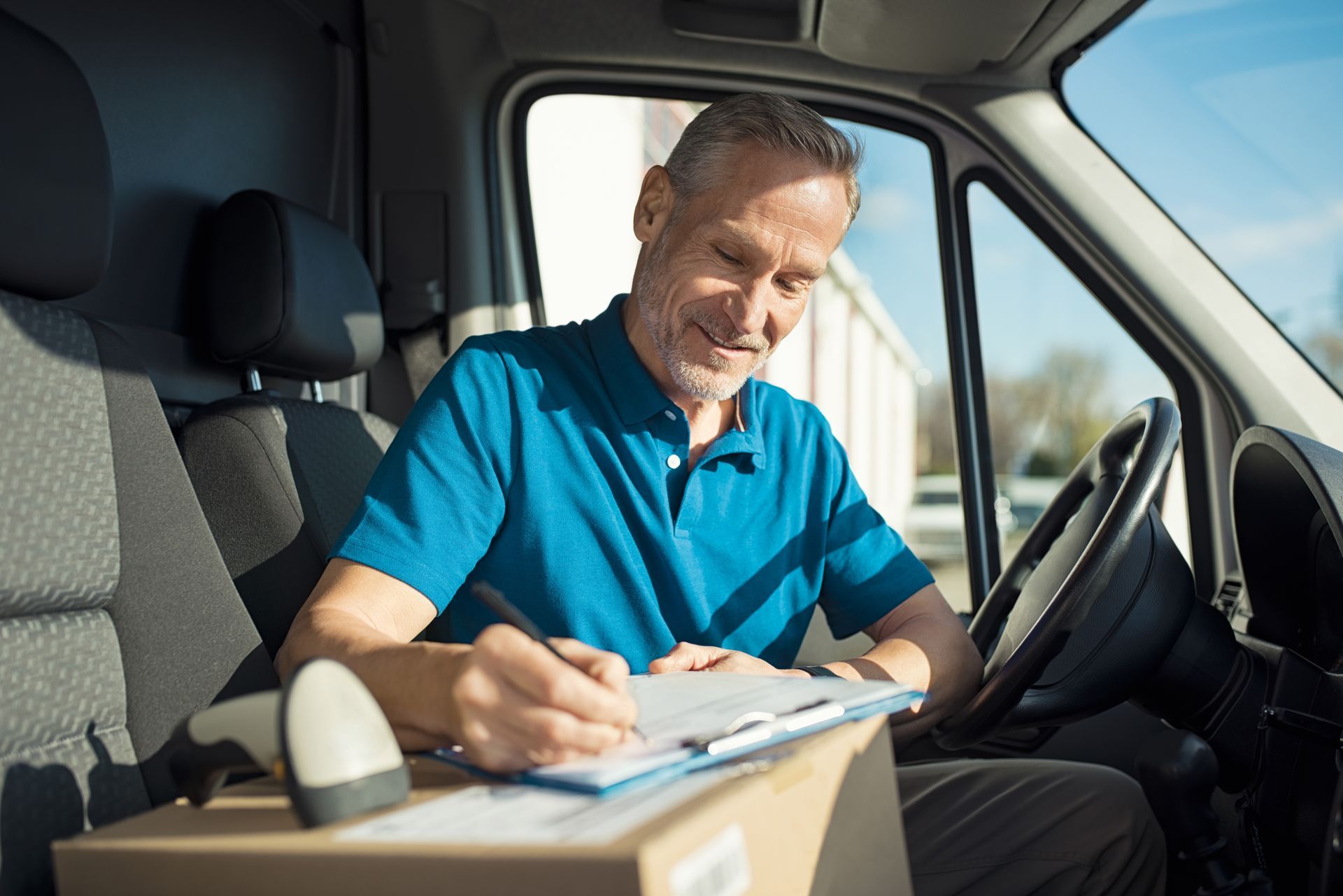 Happy delivery driver with cardboard box checking list in van