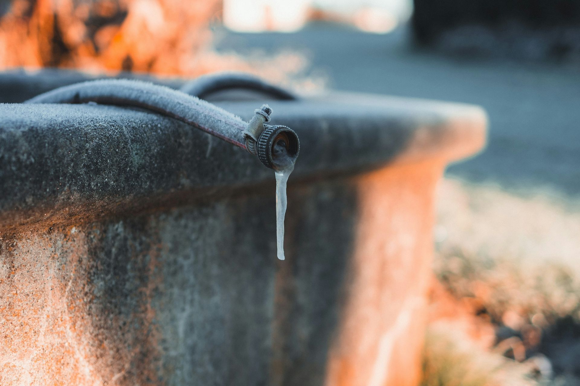 A close-up of a concrete water trough with ice forming at the spout, likely in a cold outdoor setting.