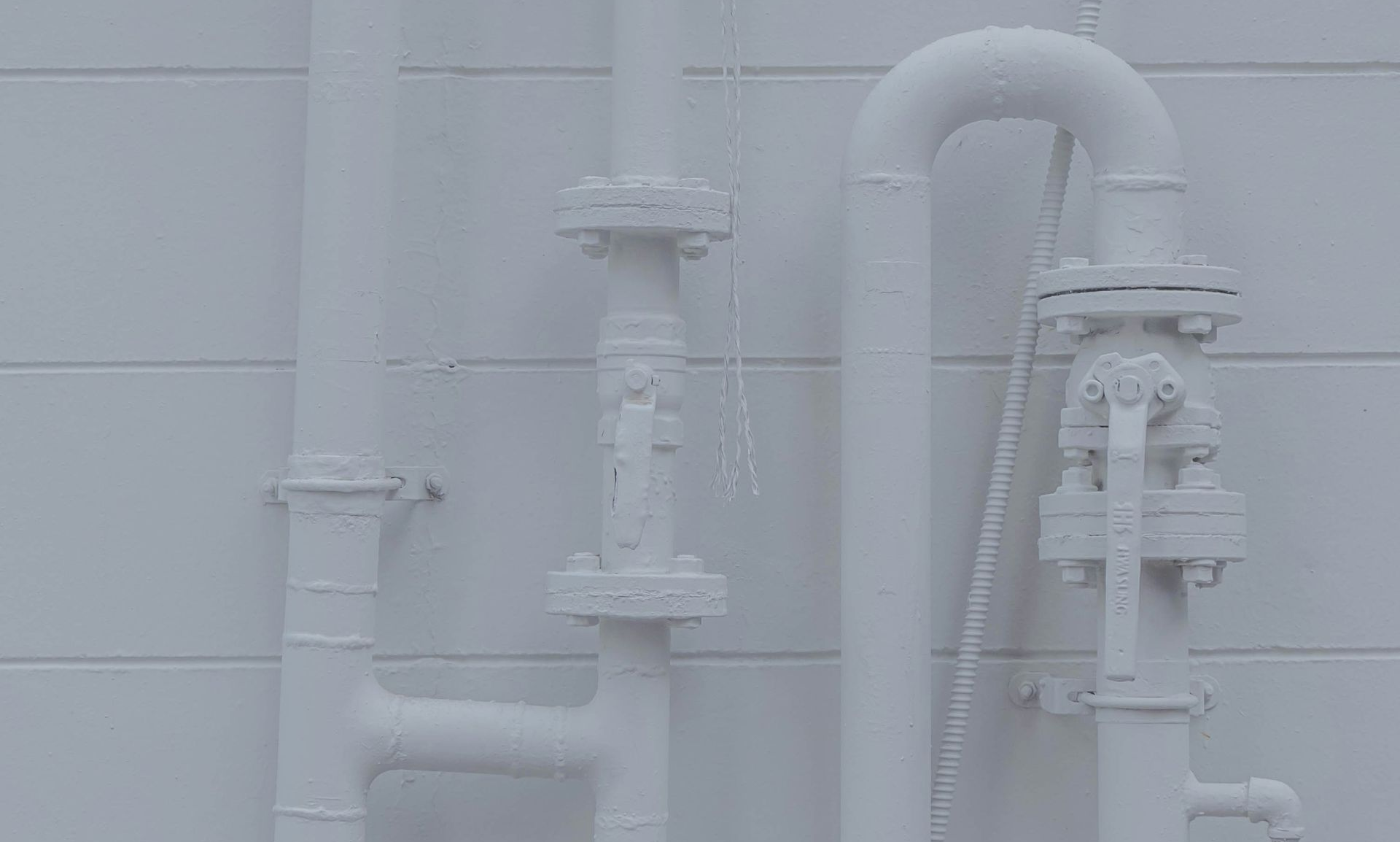 White painted pipes and valves against a white tiled wall.