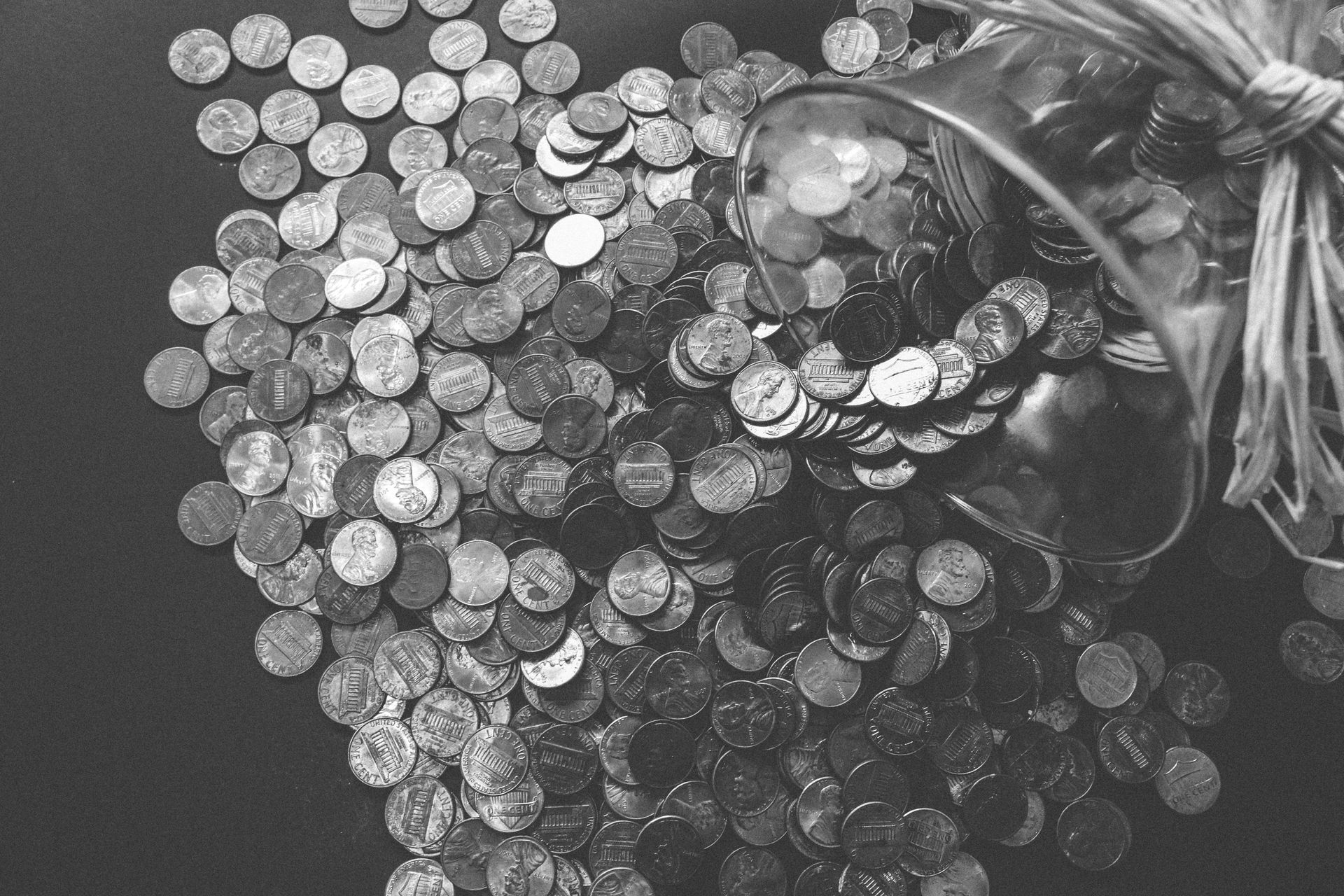 Overturned glass jar spilling pennies on a dark surface.