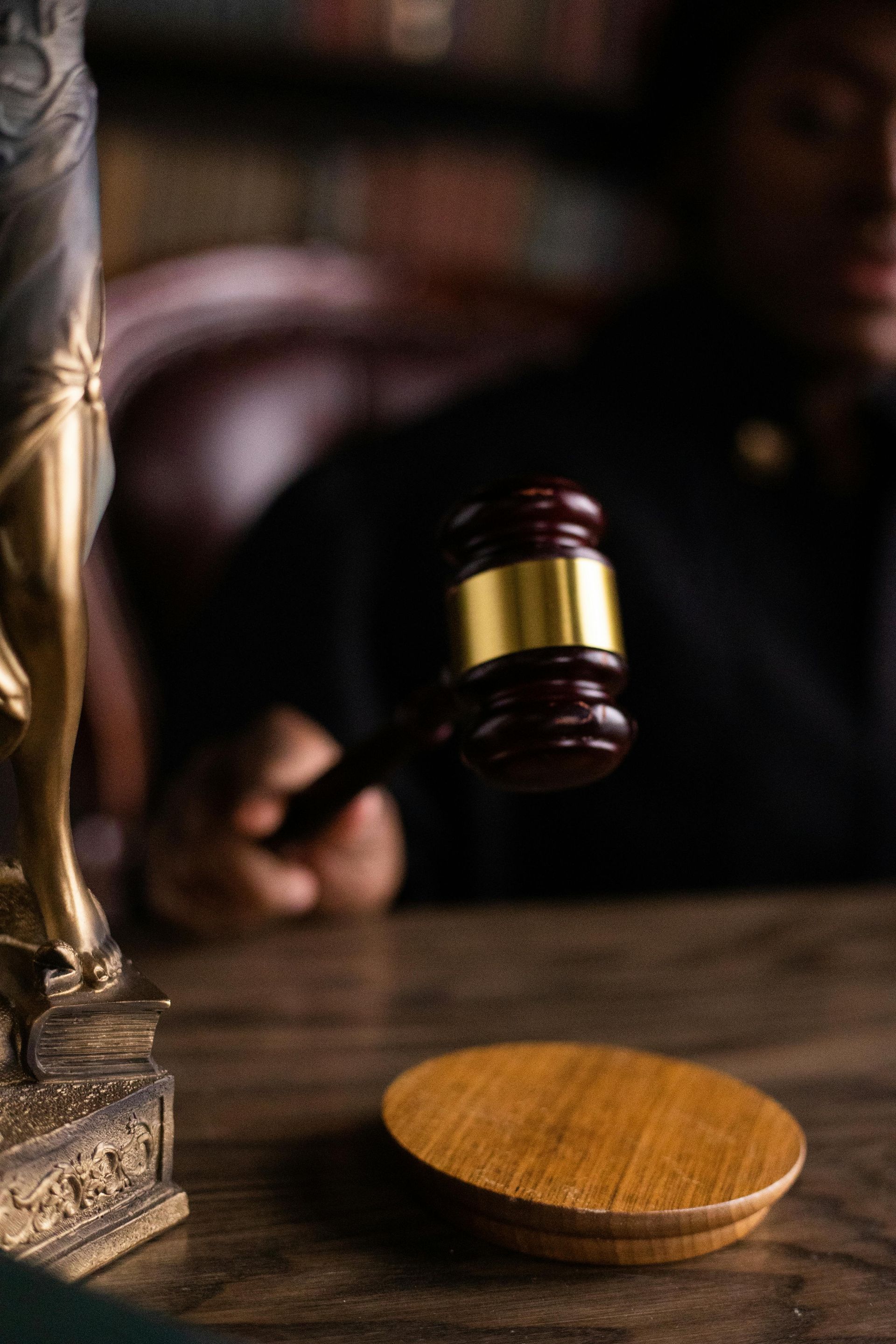 Judge holding a gavel above a wooden block, with Lady Justice statue in view.