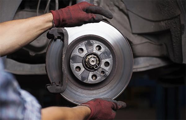 Gloved hands installing a car brake rotor and caliper on a vehicle wheel hub