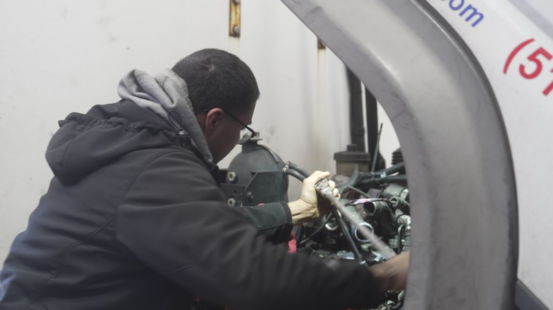 Person in a dark jacket working on machinery inside a large gray industrial machine opening