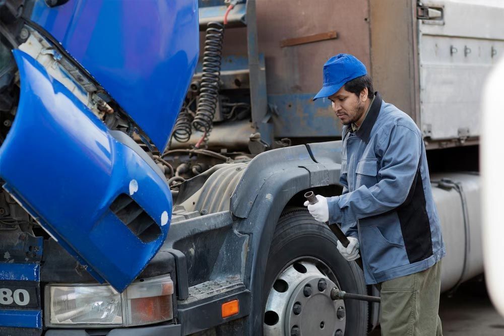 A man is working on a truck with the hood up.