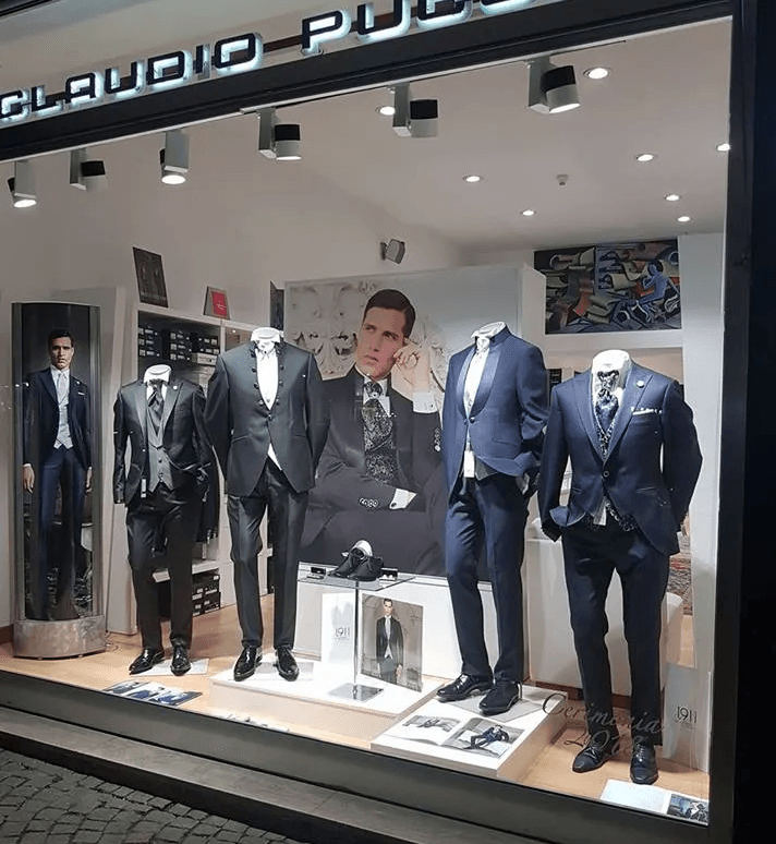 Abiti da uomo esposti nella vetrina di un negozio, con manichini che indossano abiti blu scuro e neri.