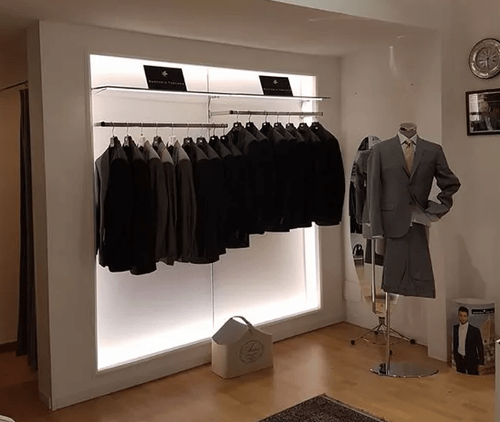 Abiti esposti su uno stand e un manichino all'interno di un negozio di abbigliamento. Pareti bianche, pavimento in legno e illuminazione soffusa.