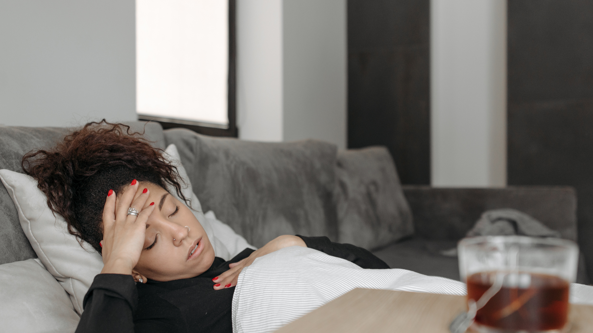 A woman is laying on a couch with her hand on her forehead.