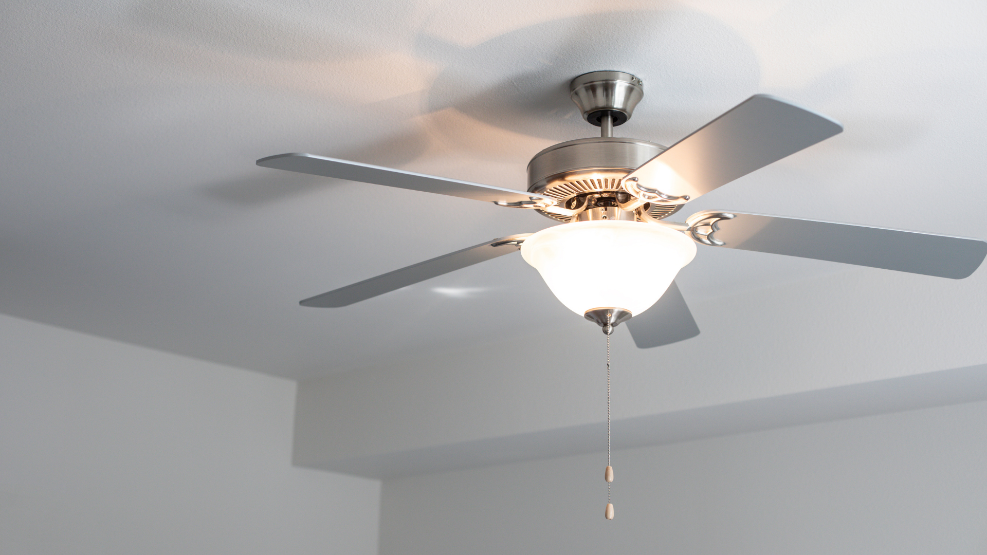 Ceiling fan with five blades and a central light fixture, mounted on a white ceiling.