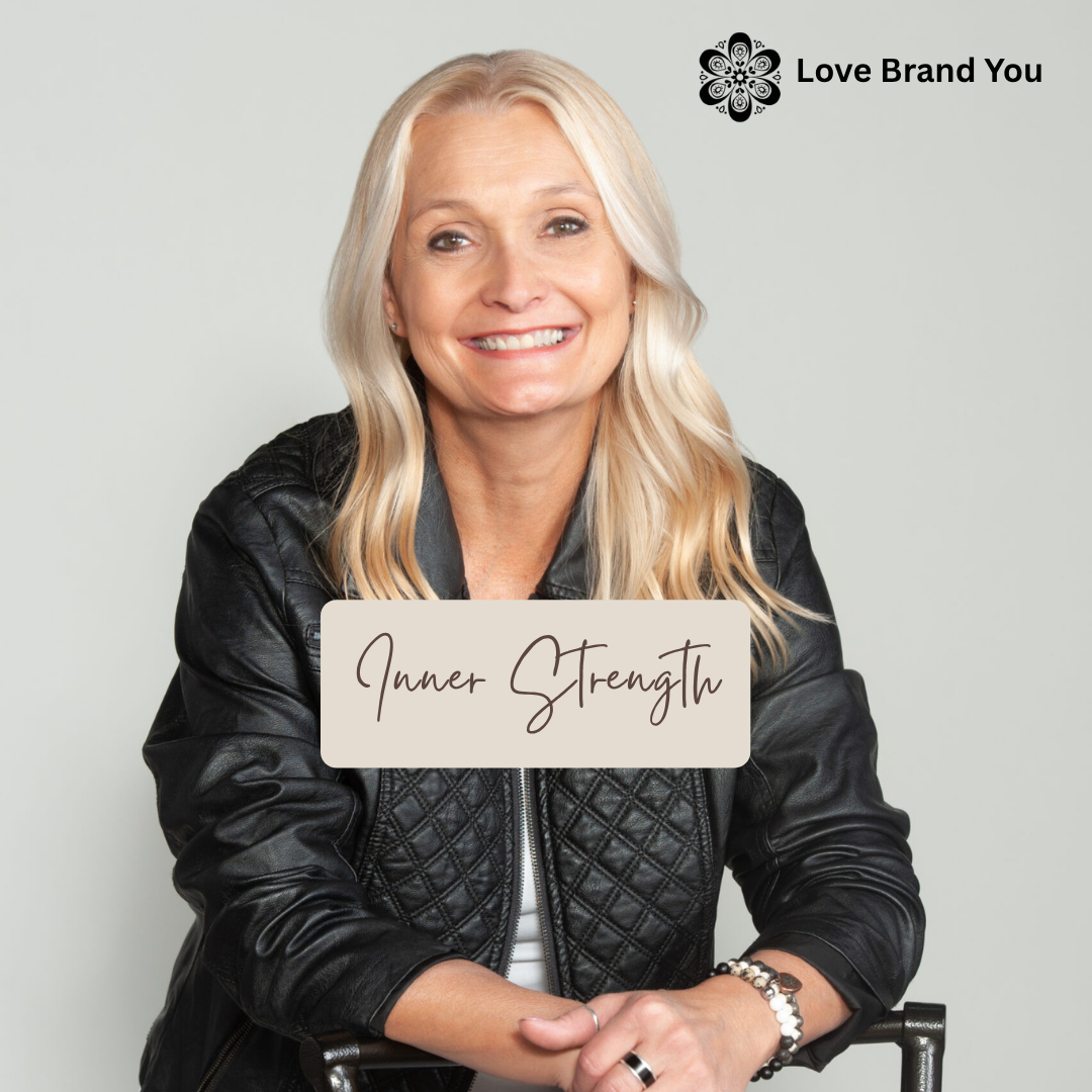 A woman in a black jacket is smiling with a sign that says inner strength