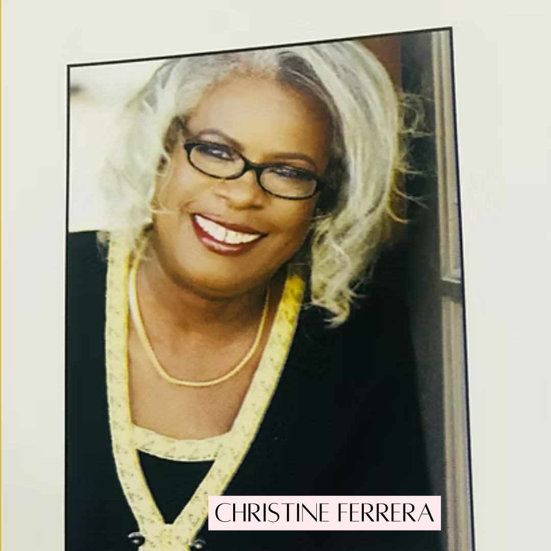 Christine Ferreira smiling, wearing glasses, black top with gold trim and a necklace.