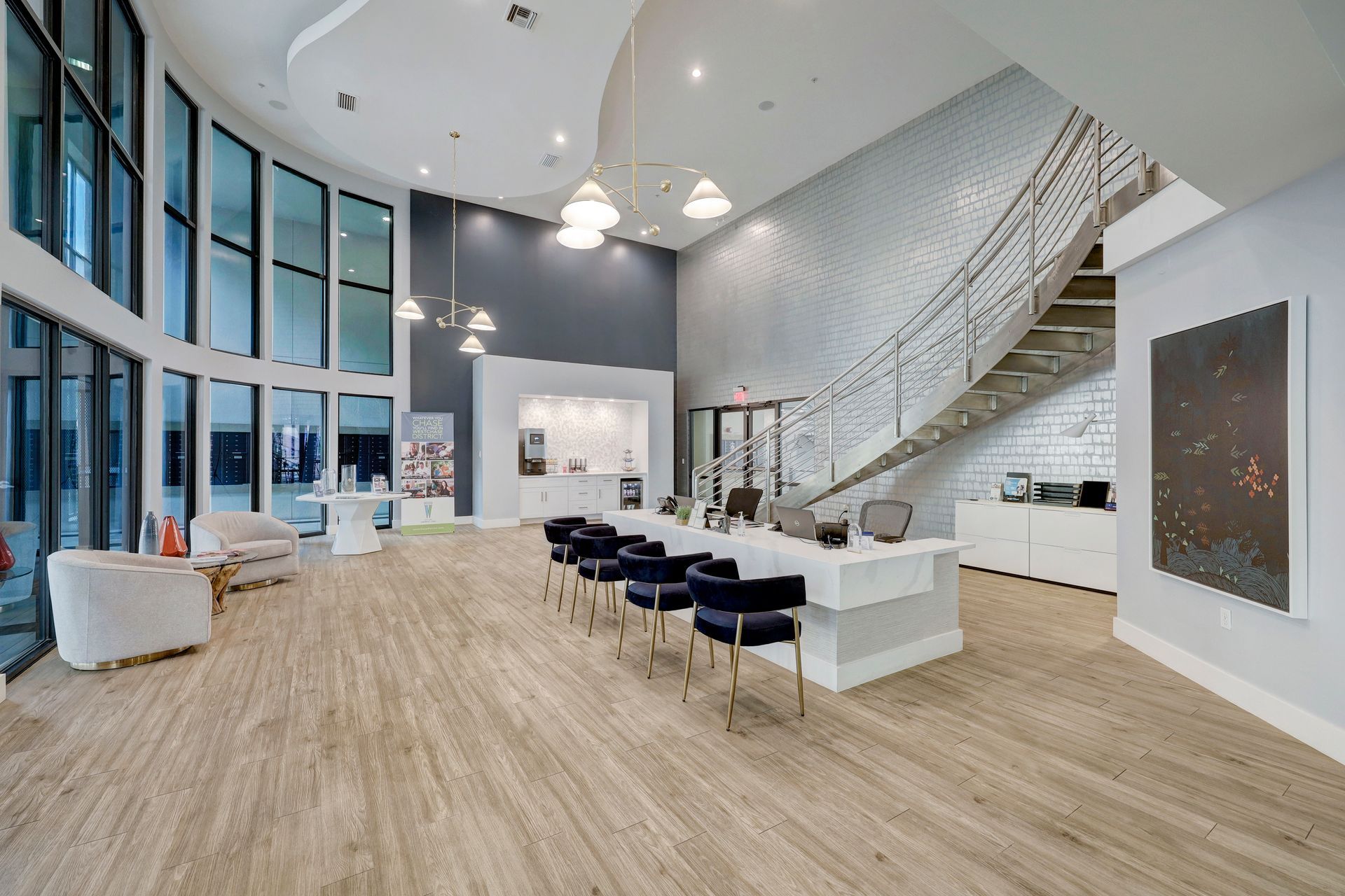 Spacious lobby with a curved glass wall, seating area, reception desk, and staircase.