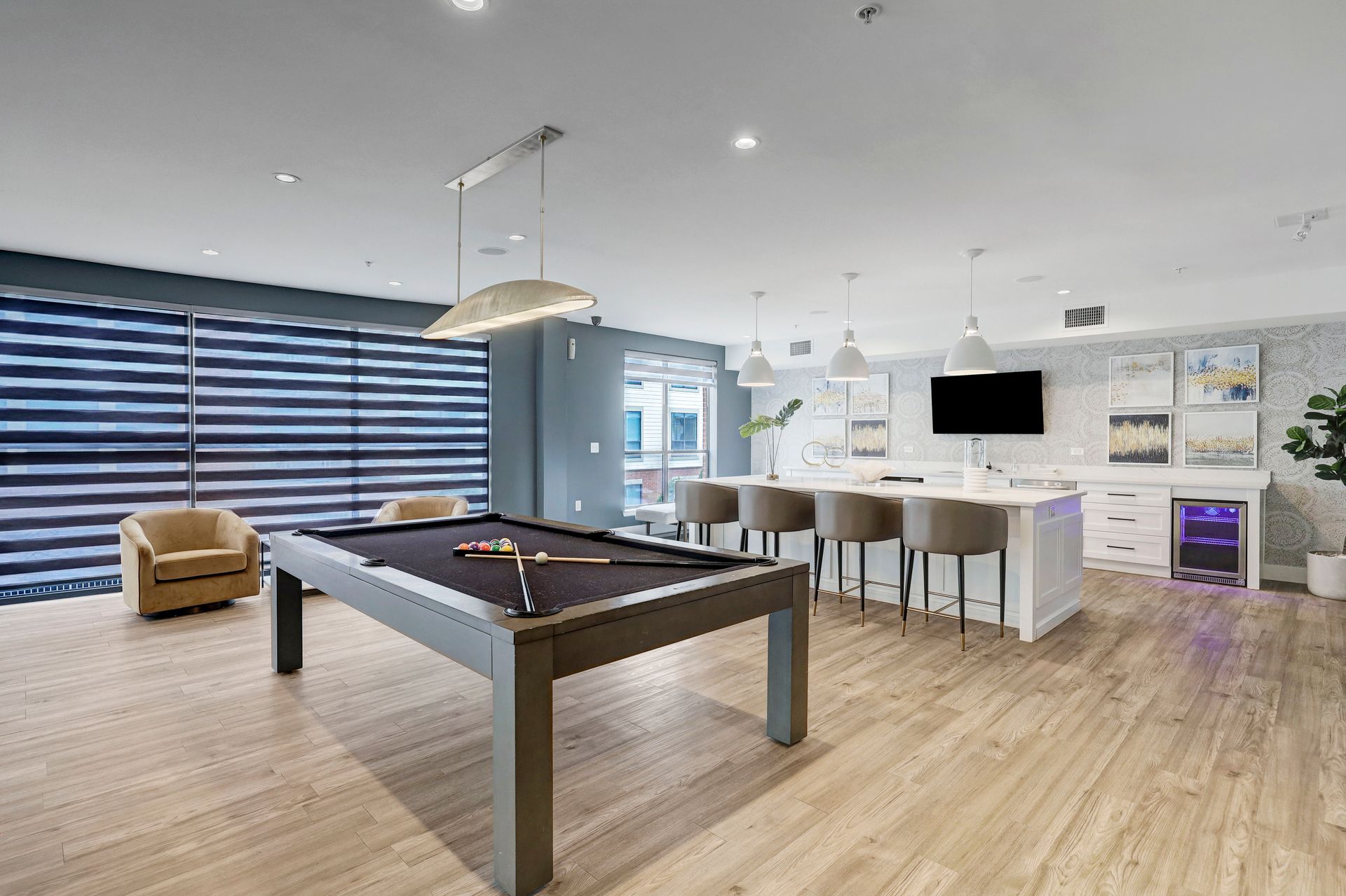 Game room with pool table, bar seating, and wall-mounted TV. Neutral tones, blue accents, and a large window.