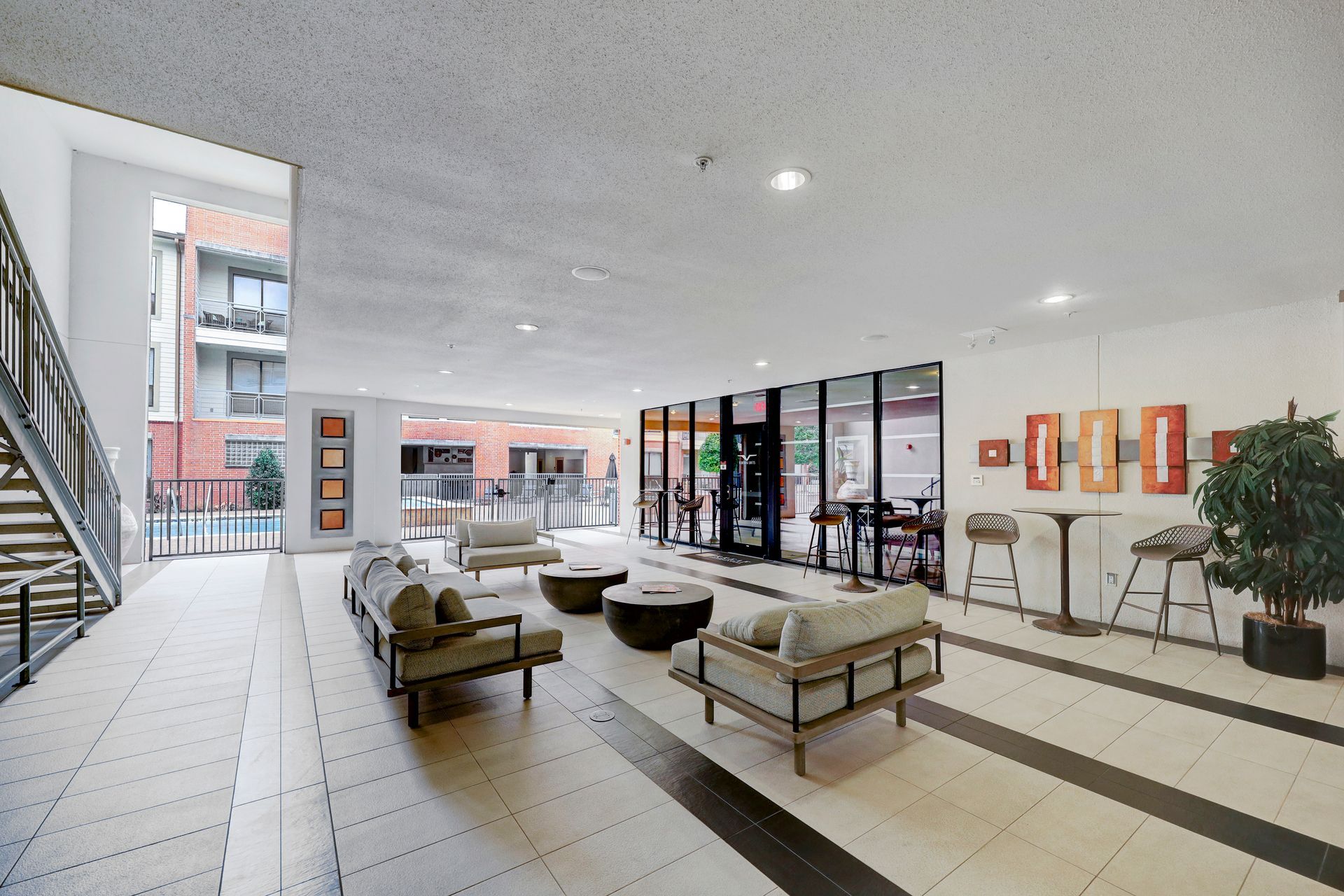 Lounge area with couches, coffee tables, and fitness center visible through glass walls. Neutral colors, modern design.